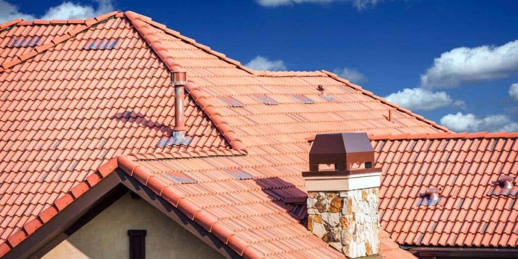 Terracotta roofing materials with a chimney under a clear blue sky with fluffy white clouds.