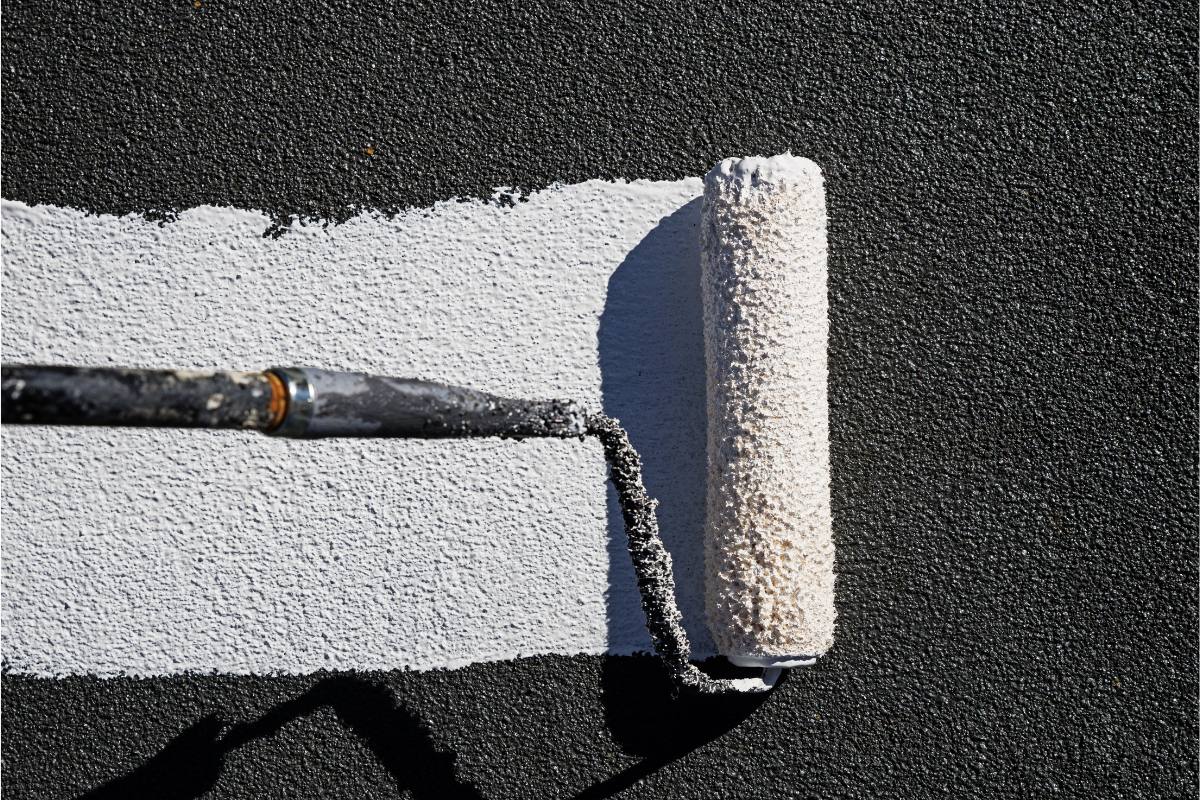 A close-up of a roller applying white coating on a black rooftop surface.