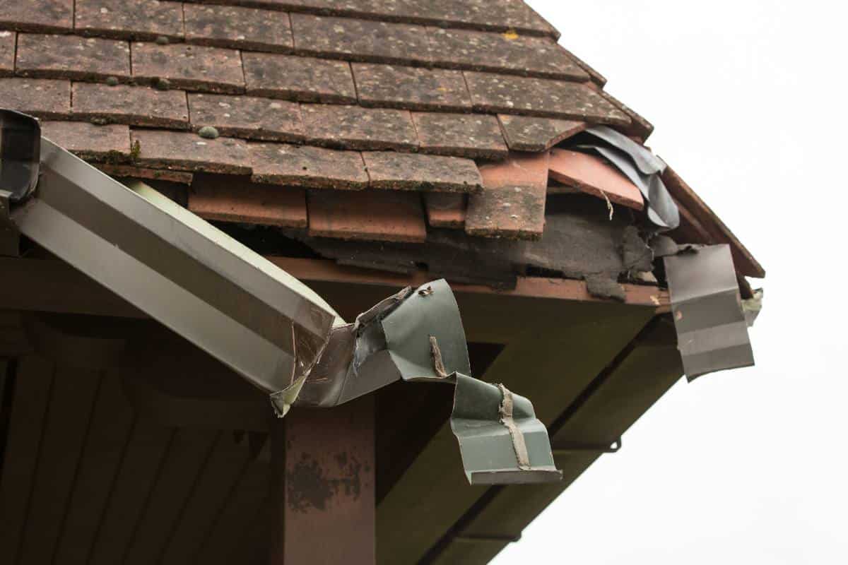 Damaged gutter and roof tiles on a house, indicating the need for repair.