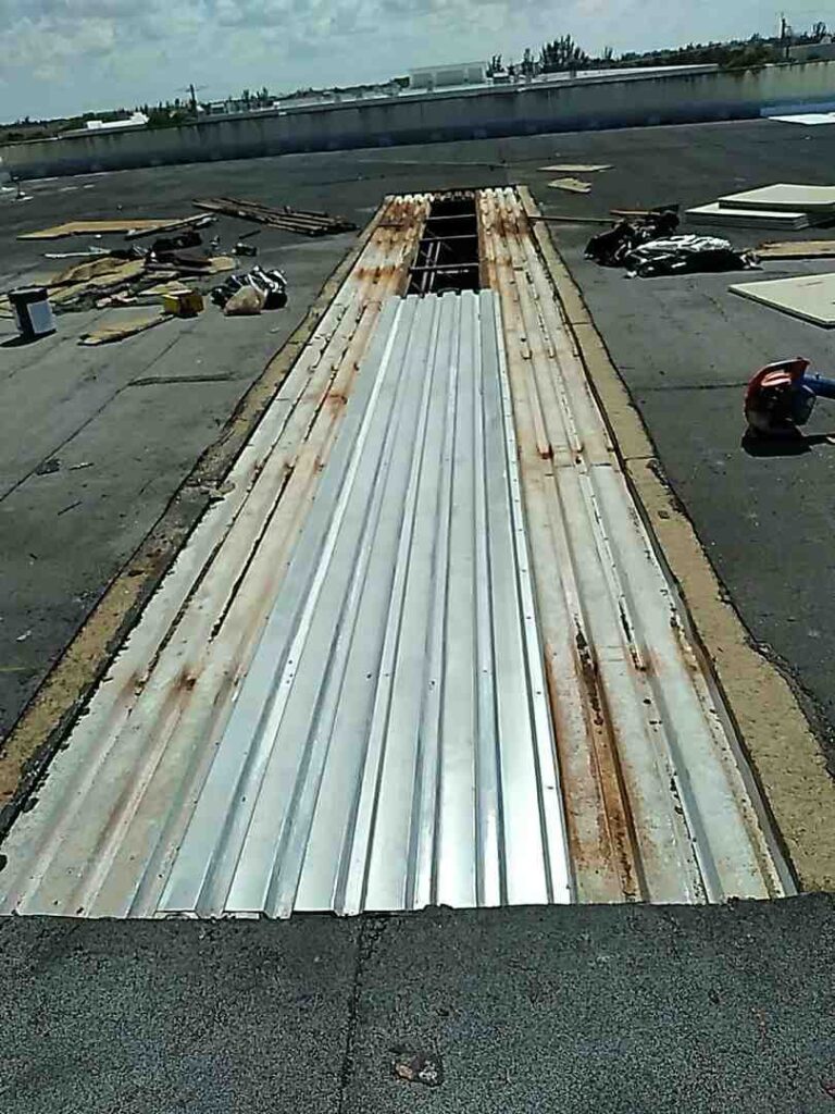 Rusty metal roofing panel with wood framing and construction tools on rooftop during repair.