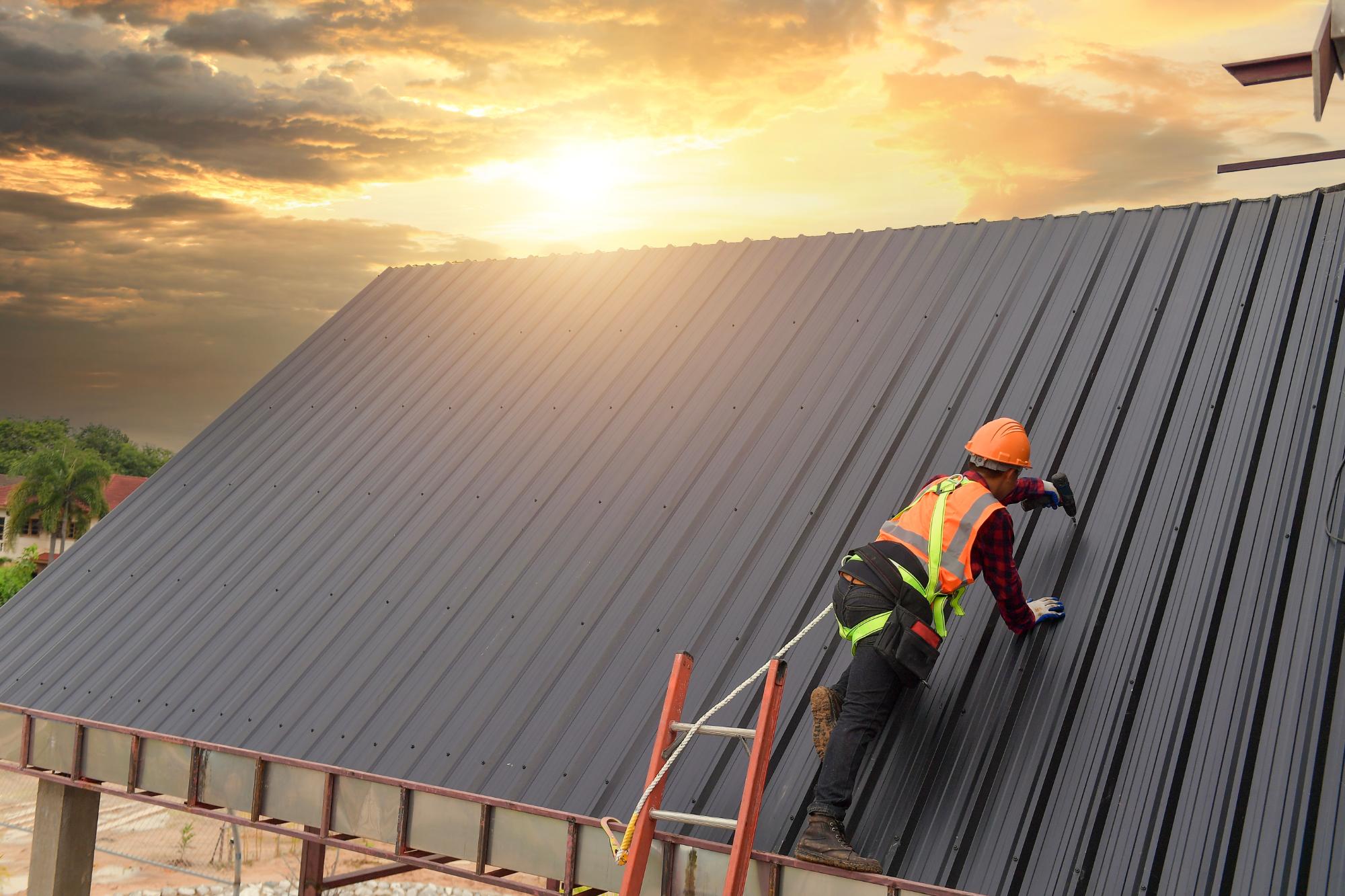 A construction worker wearing safety gear and a harness installs or inspects metal roofing sheets on a sloped roof at sunset, with a dramatic sky in the background.